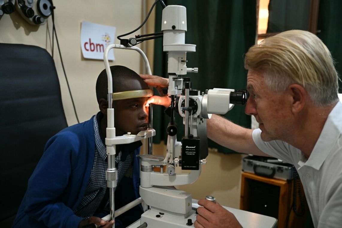 Ein Mann schaut durch ein großes Augenmikroskop in die Augen eines Kindes.